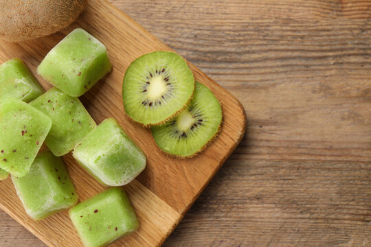 Frozen kiwi puree cubes and ingredient on wooden table, top view. Space for text