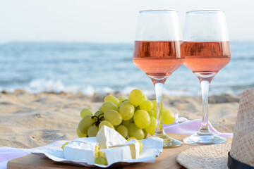Glasses with rose wine and snacks on sandy seashore, closeup. Space for text