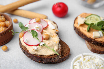 Delicious sandwiches with hummus and different ingredients on light grey table