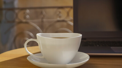 Cup of aromatic coffee and laptop on wooden table outdoors, closeup