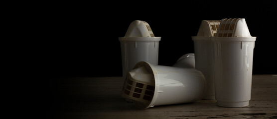 Horizontal banner with plastic used water filters on black background. Photo in low key. Concept of drinking water purification, environmental awareness, garbage sorting, recycling. Ecological crisis