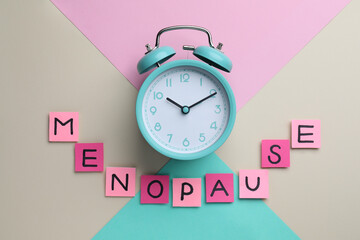 Pink paper notes with word Menopause and alarm clock on color background, flat lay