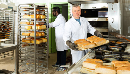 Confident bakery worker arranging trays with freshly baked loaves..