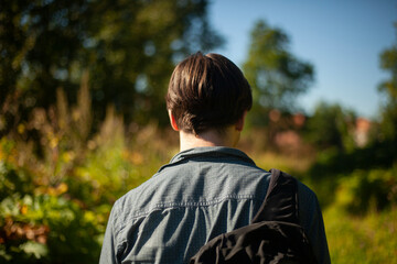 Guy walks through woods. Man from behind in summer. Young man came to village.