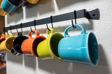 A collection of colorful mugs hanging on black hooks against a white wall