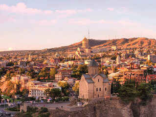 Fototapeta premium Summer sunset view on historic neighbourhood of Avlabari in capital of Georgia Tbilisi Tiflis city with Metekhi St. Virgin Church erected on steep bank of Mtkvari Kura river in foreground and Holy