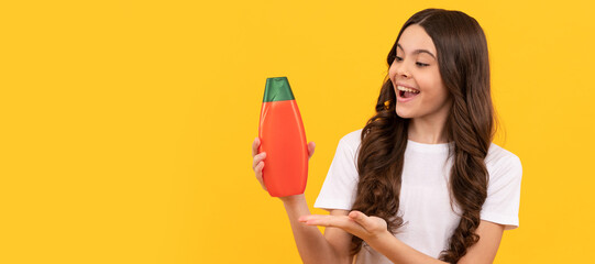 happy kid with long hair presenting product of shampoo bottle, product proposal. Banner of child girl hair care, studio poster header with copy space.