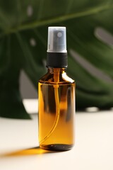 Spray bottle with oil and green leaf on white table. Natural cosmetics