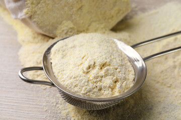 Sieve with quinoa flour on wooden table, closeup