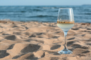 Glass of tasty wine on sand near sea, space for text