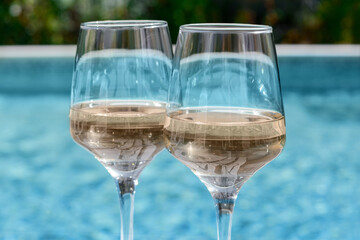 Glasses of tasty wine near swimming pool, closeup
