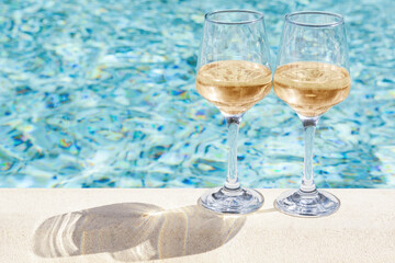 Glasses of tasty wine on swimming pool edge, space for text