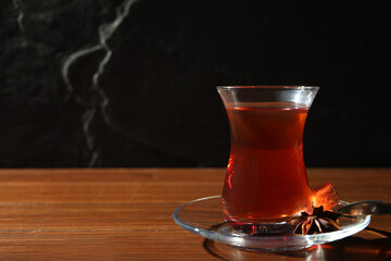 Glass of traditional Turkish tea on wooden table against black background. Space for text