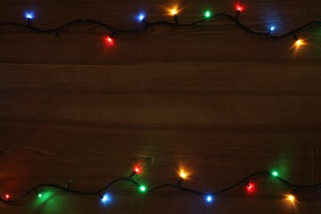 Frame of colorful Christmas lights on wooden table, top view. Space for text