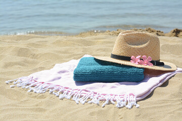 Blanket with towel, stylish straw hat and flowers on sand near sea, space for text. Beach...