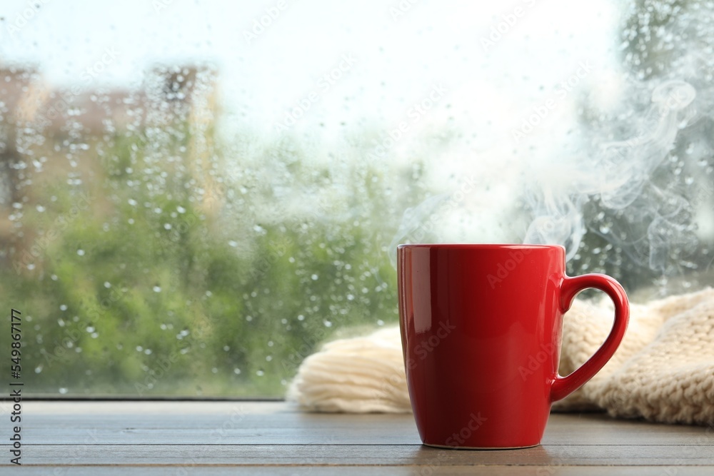 Poster Cup of hot drink and knitted plaid near window on rainy day. Space for text