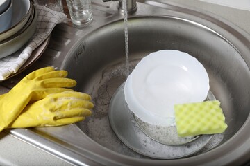 Washing plates, sponge and rubber gloves in kitchen sink