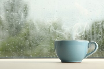 Obraz na płótnie Canvas Cup of hot drink near window on rainy day. Space for text