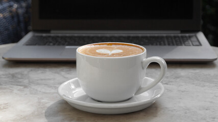 Cup of delicious coffee and laptop on beige marble table outdoors