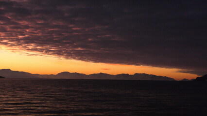 Popcorn clouds illuminated pink over the silhouette of a mountain, at sunset at Cierva Cove, Antarctica