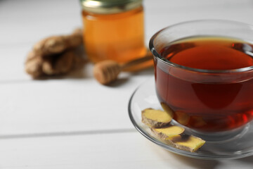 Cup of delicious ginger tea and ingredients on white wooden table, closeup. Space for text