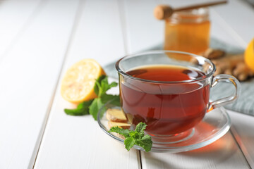 Cup of delicious ginger tea and ingredients on white wooden table, closeup. Space for text
