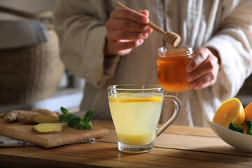 Woman making aromatic ginger tea at wooden table indoors, closeup