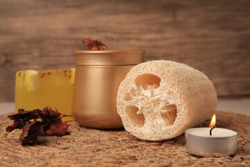 Natural loofah sponge, cosmetic products and candle on wicker mat, closeup