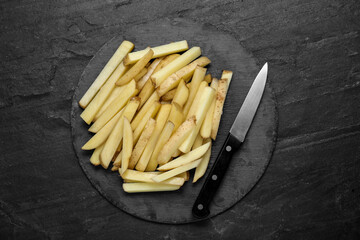 Cut raw potatoes with knife on black table, top view