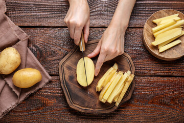 Woman cut potatoes at wooden table, top view