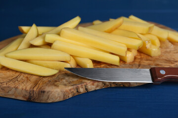 Cut raw potatoes and knife on blue wooden table, closeup. Cooking delicious French fries