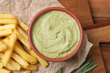 Serving board with parchment, french fries, avocado dip and rosemary on wooden table, top view