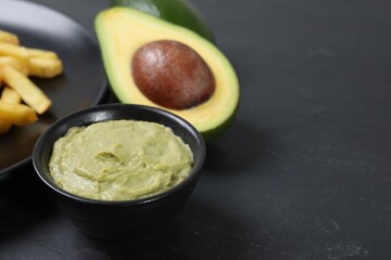 Plate with french fries, guacamole dip and avocado served on black table, closeup. Space for text
