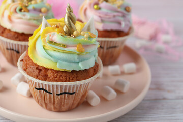 Plate with cute sweet unicorn cupcakes on white wooden table, closeup