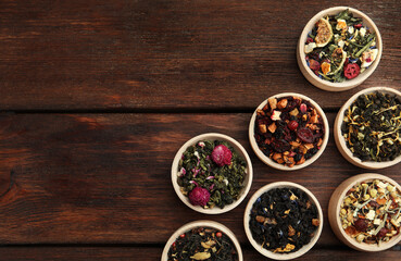 Different kinds of dry herbal tea in bowls on wooden table, flat lay. Space for text