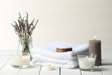 Beautiful composition with burning candles and different spa products on white wooden table