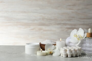 Beautiful composition with different spa products, burning candles and flowers on light grey table. Space for text