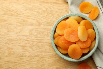 Bowl of tasty apricots on wooden table, top view and space for text. Dried fruits