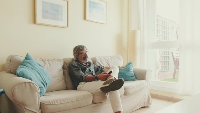 Elderly man with tv remote control sitting on sofa at home