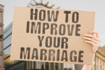 The phrase " How to Improve Your Marriage " is on a banner in men's hands with blurred background. Love. Spouse. Wife. Family. Female. Girlfriend. Husband. Lover. Relationship. Romantic. Boyfriend