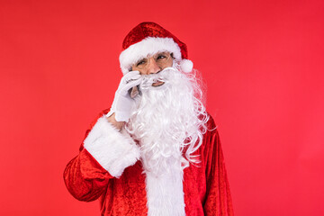 Man dressed as Santa Claus, talking on his mobile phone, on red background. Christmas, celebration, gifts, consumerism and happiness concept.