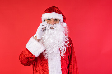 Man dressed as Santa Claus, talking on his mobile phone, on red background. Christmas, celebration, gifts, consumerism and happiness concept.