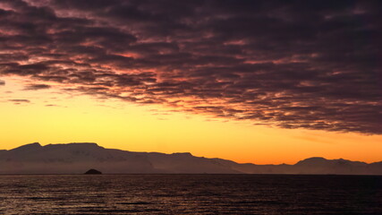 Popcorn clouds illuminated pink over the silhouette of a mountain, at sunset at Cierva Cove, Antarctica
