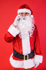 Man dressed as Santa Claus, talking on his mobile phone, on red background. Christmas, celebration, gifts, consumerism and happiness concept.