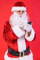 Man dressed as Santa Claus, consulting his mobile phone, on red background. Christmas, celebration, gifts, consumerism and happiness concept.