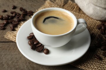 Cup of aromatic coffee and beans on wooden table