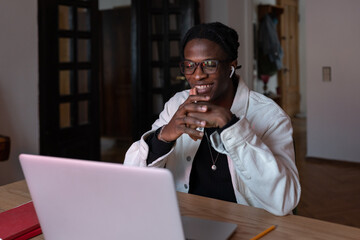 Fototapeta na wymiar Young smiling African American man remote worker in eyewear looking at laptop screen reading e-mail, receiving job offer, working remotely on computer, sitting at table at home office, selective focus