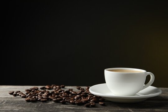 Cup of hot aromatic coffee and roasted beans on wooden table against dark background, space for text © New Africa