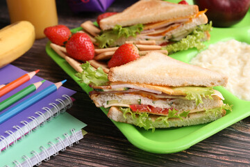 Serving tray of healthy food and stationery on wooden table, closeup. School lunch