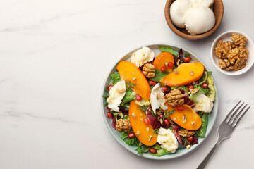 Delicious persimmon salad with cheese and pomegranate served on white marble table, flat lay. Space for text